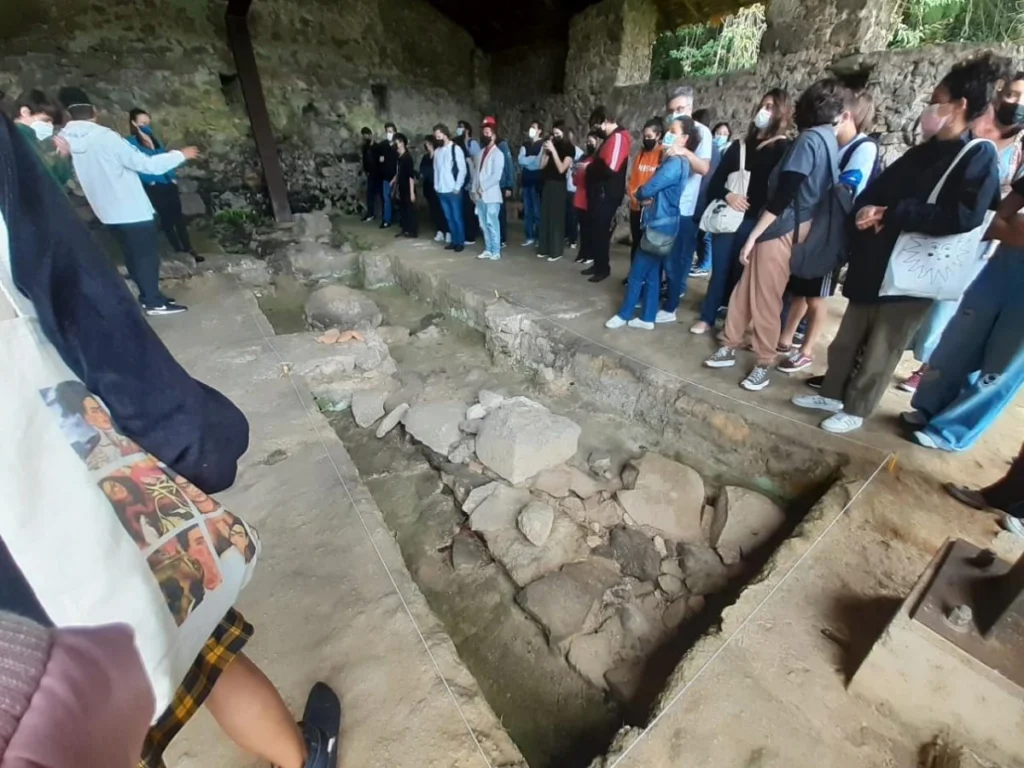 Grupo de pessoas participando de atividade cultural ao lado de uma ruína histórica em uma cidade pequena.