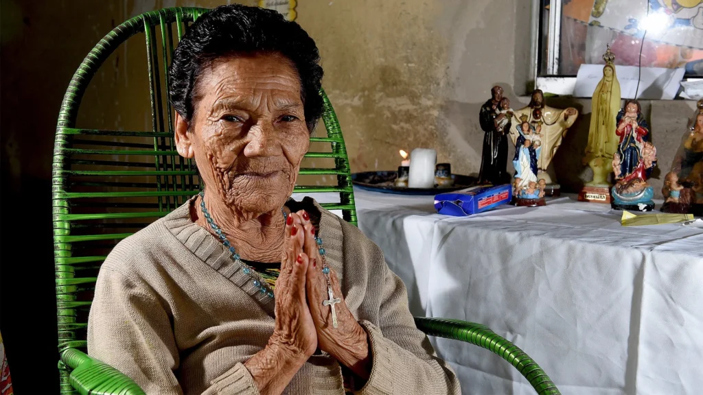 Benzedeira idosa com véu e terço nas mãos, representando as guardiãs da fé e tradição no interior brasileiro.