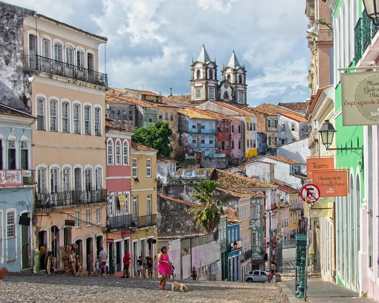 Rua com casas coloridas de arquitetura colonial no Pelourinho, com detalhes ornamentados e sacadas de ferro, refletindo o ambiente histórico de Salvador.