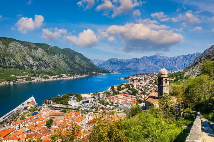 Vista da Baía de Kotor ao entardecer, com a cidade antiga e as montanhas refletidas nas águas calmas.